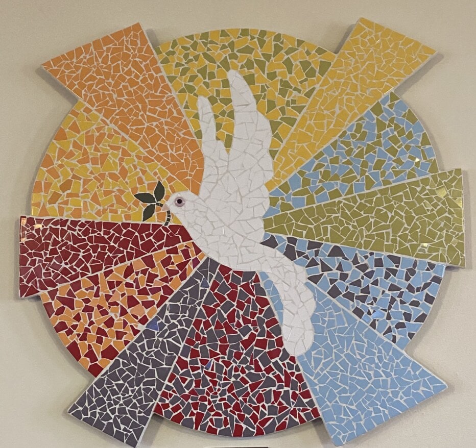 Mosiac artwork of a white dove holding an olive branch flying in front of a multicolored sun.