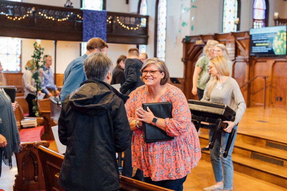 A woman extends her hand in greeting to another person at church