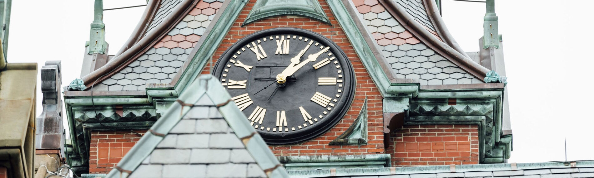 A clock on the steeple of a brick church with slate roof