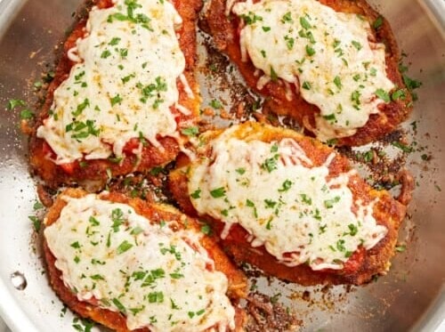 Four pieces of Chicken Parmesan in a frying pan