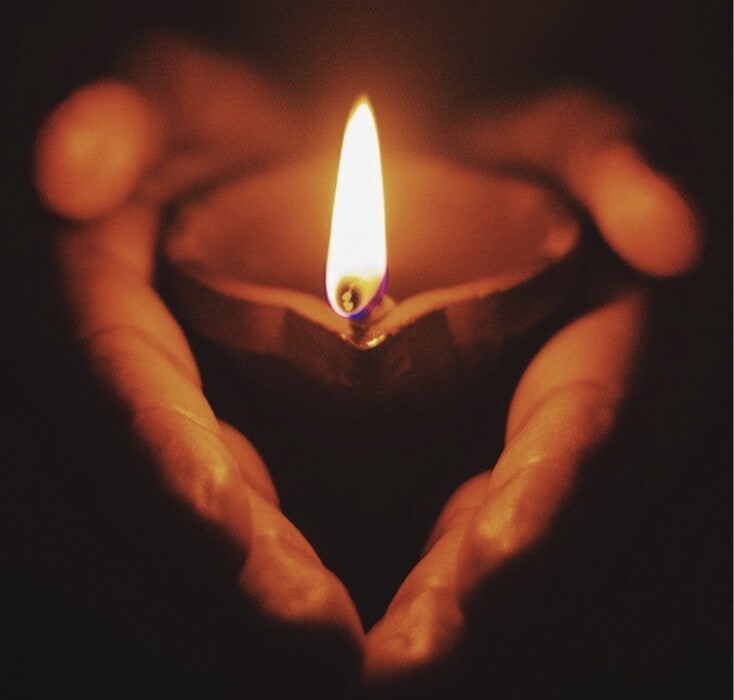 Two hands cupping a small light candle.